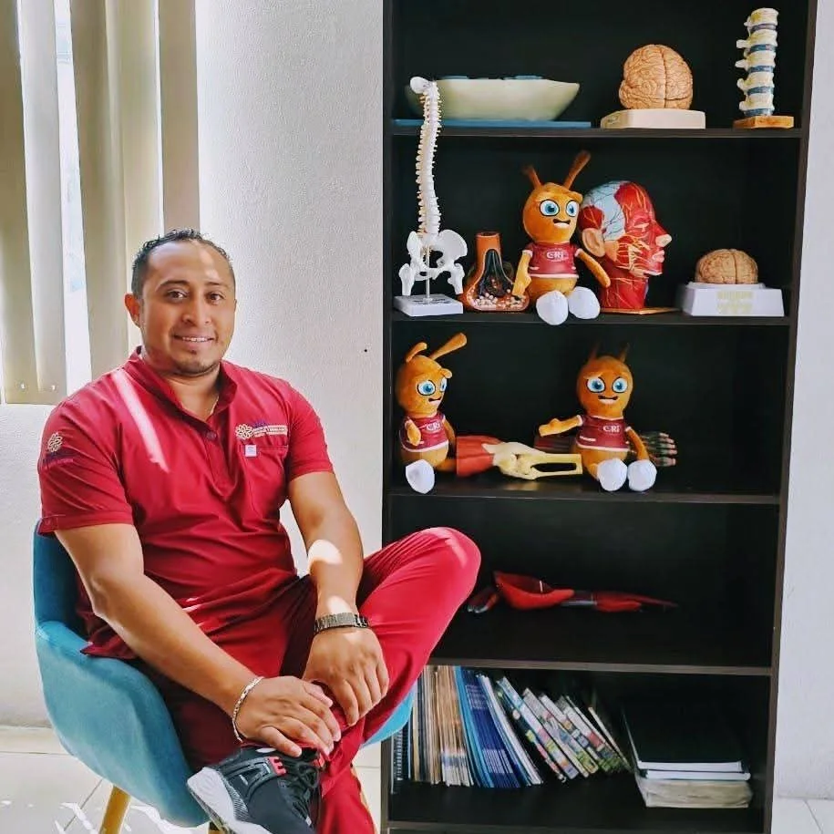 Miguel Ángel Colorado sentado en su consultorio junto a modelos anatómicos